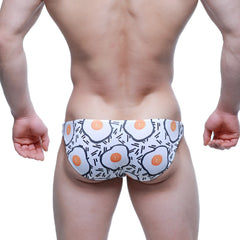 White swim trunks by metromalewear featuring a playful cartoon-style fried egg pattern with orange yolks and black outlines
