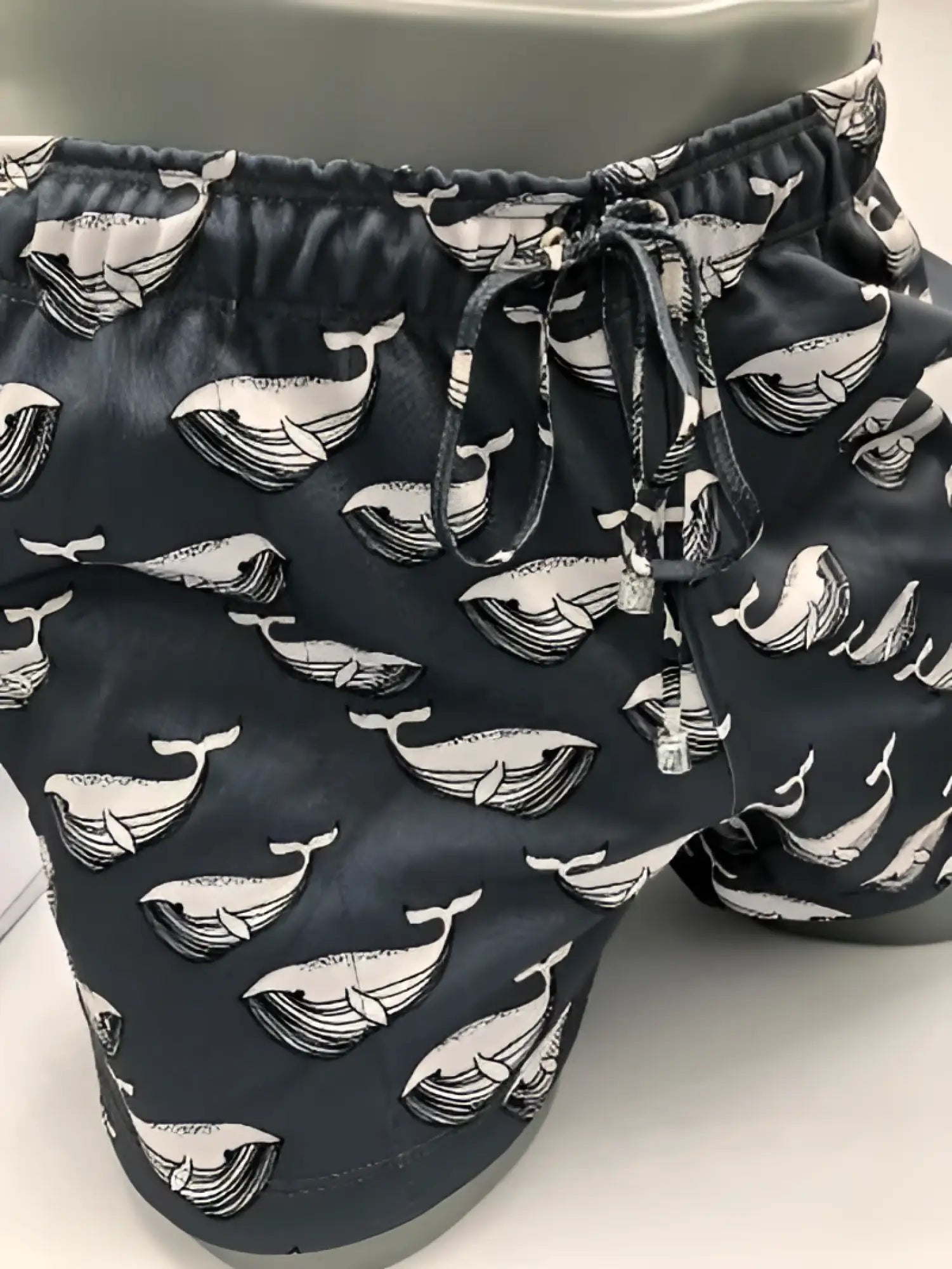 Black swim trunks featuring a repeating white whale pattern with detailed line art from moby dick shorts collection