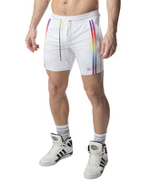 A model wears white Nasty Pig Aura Pride rugby shorts with rainbow side stripes and matching drawstrings.