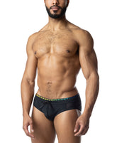 A muscular model wears Nasty Pig Prism Pride black bikini swimwear with a rainbow-accented waistband against a white background.