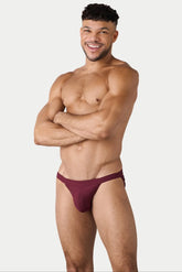 A smiling man wearing maroon ribbed swim tangas with arms crossed, against a plain white background.