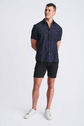 Man wearing a navy short-sleeve jacquard shirt, black shorts, and white sneakers against a light background.