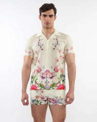 A man wearing a cream printed short sleeve woven modal border shirt with vibrant floral and butterfly patterns