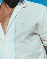 White santorini linen shirt with light blue embroidered detailing along the placket and matching logo on the chest