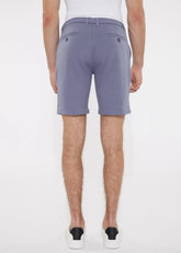 A pair of solid stretch knit shorts in soft lavender with lightweight fabric and dark button accents on back pockets backside view