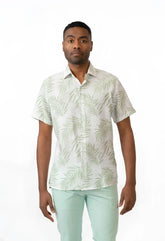 A man wearing a summer rain s s shirt with light green palm leaf pattern on off white short sleeved button up shirt