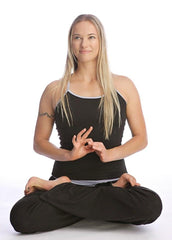 Woman wearing a black sustain yoga halter top sitting cross-legged with hands forming a mudra in loose pants