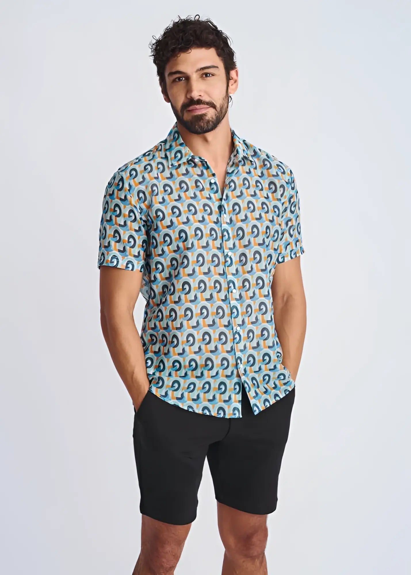 A man wearing a swirls lightweight cotton silk short-sleeved shirt with blue teal and orange geometric pattern