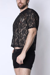 Man wearing a black floral lace cropped tee and black shorts against a plain white background.