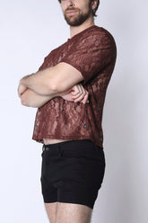 A man wearing a rust-colored Timoteo Sorrento lace cropped tee and black shorts, posed with arms crossed.