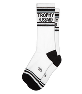 White athletic crew socks with black stripes and trophy husband text on cuff featuring a small logo near the toe