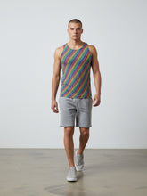 A male model walks forward wearing a Tulio Swimwear rainbow dots tank top, grey shorts, and sneakers.