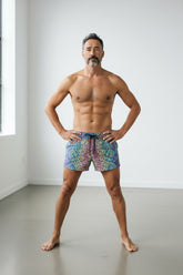 Man posing in multicolored rainbow maze patterned linen texture shorts with drawstring waist.