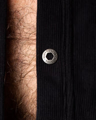 A silver-toned hexagonal snap button engraved with musty pig inc on ribbed black fabric of a union suit garment