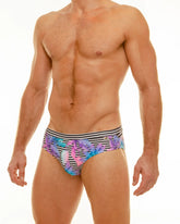 Wild mango swim brief men’s trunks with vibrant purple pink and blue tropical leaf pattern on black and white stripes