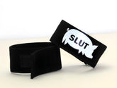 Black velour wristband with white embroidered speech bubble reading slut in bold black letters from wildmant fetish max cock-ring-pig slut collection
