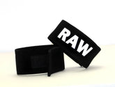 Black fabric wrist wraps with bold white raw lettering from wildmant fetish max cock-ring-raw product line