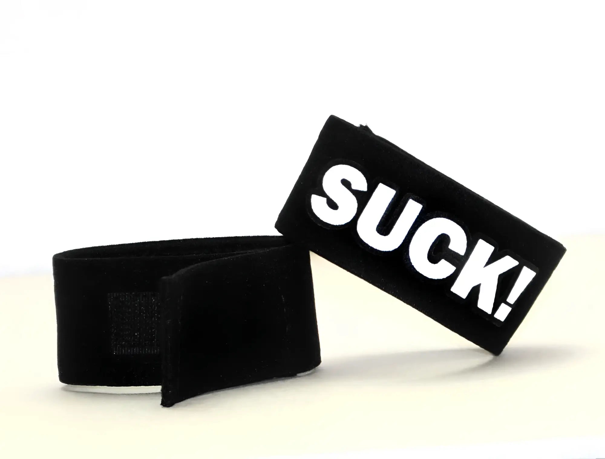 Black velour wristband with bold white suck lettering from wildmant fetish max cock ring suck product line