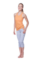 A woman wearing a soft orange all american racerback tank top paired with light gray capri pants