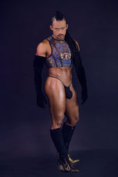 Muscular man in a bold, colorful crop top, black thong, long gloves, and ornate boots.