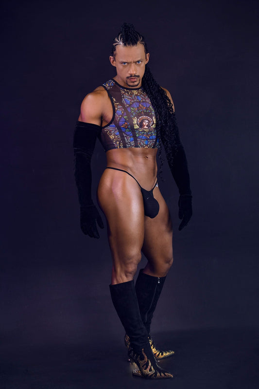Muscular man in a bold, colorful crop top, black thong, long gloves, and ornate boots.