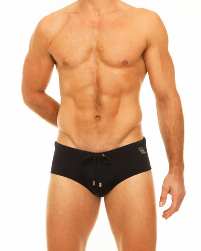 A shirtless man wears black swim briefs with a drawstring on white.