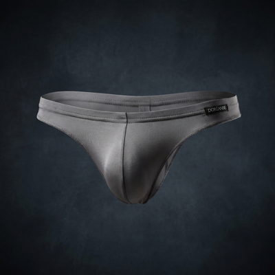 Silver-grey satin men's thong with Doréanse waistband label, product shot on dark blue-grey background