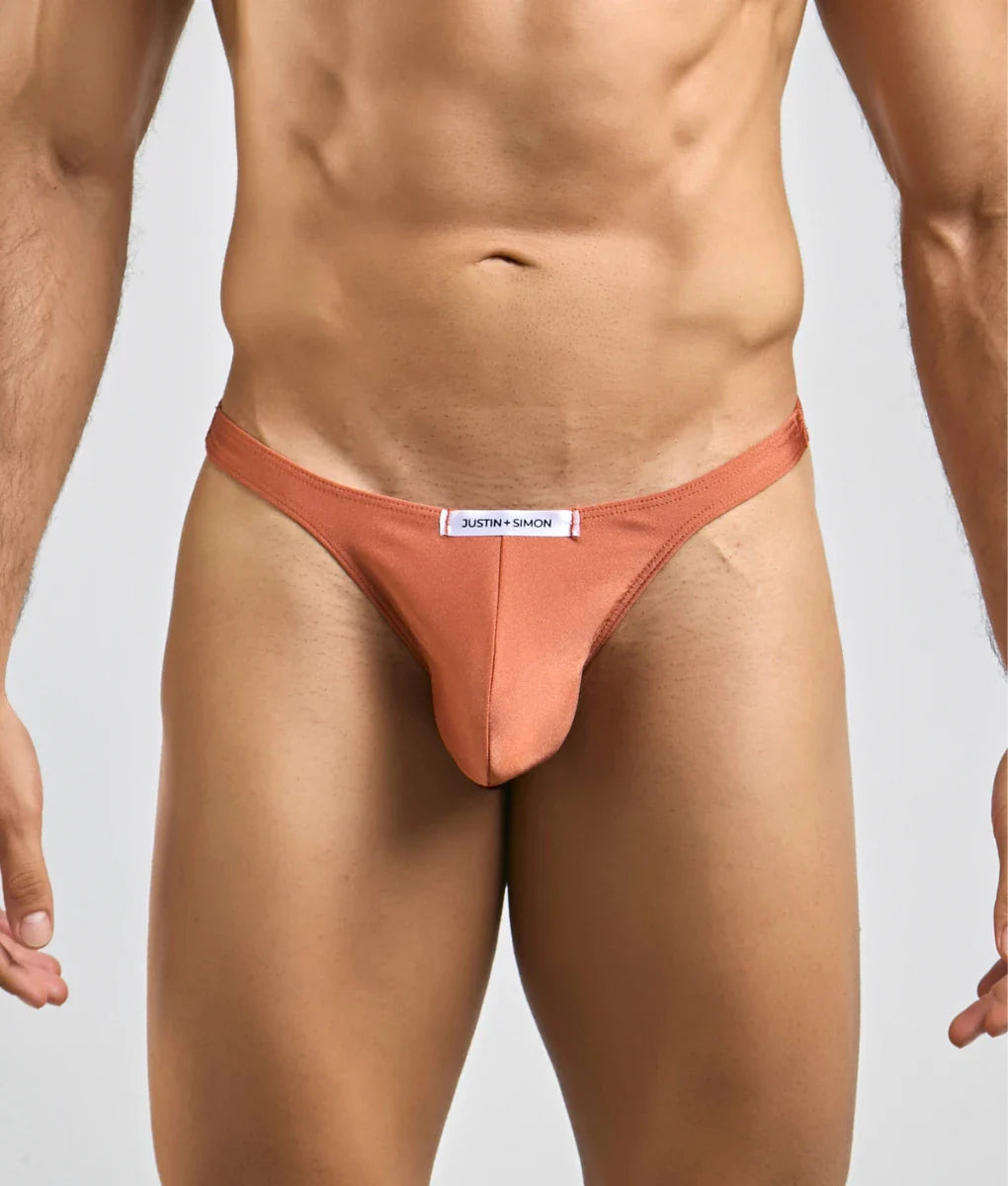 A sleek peach-colored justin simon classic tanga thong made of smooth form-fitting fabric with a branded waistband