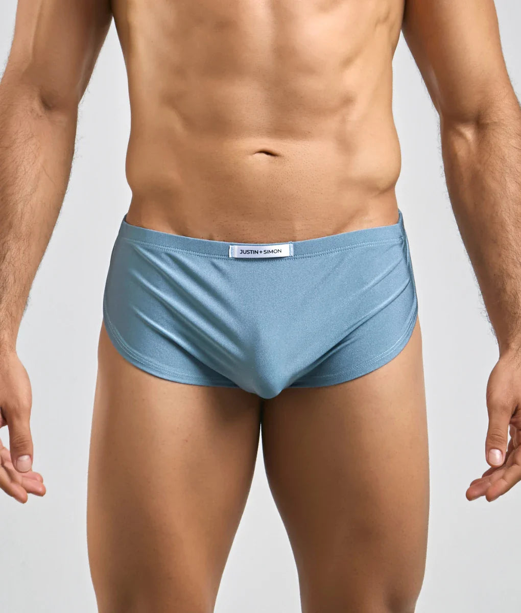 Light blue form-fitting justin + simon running short briefs with subtle sheen and white brand tag at the waistband