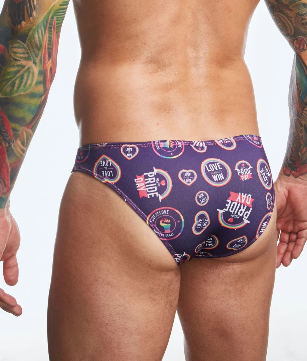 Purple swim trunks with vibrant rainbow-colored pride day logos and text in justin simon classic mens bikini fun prints