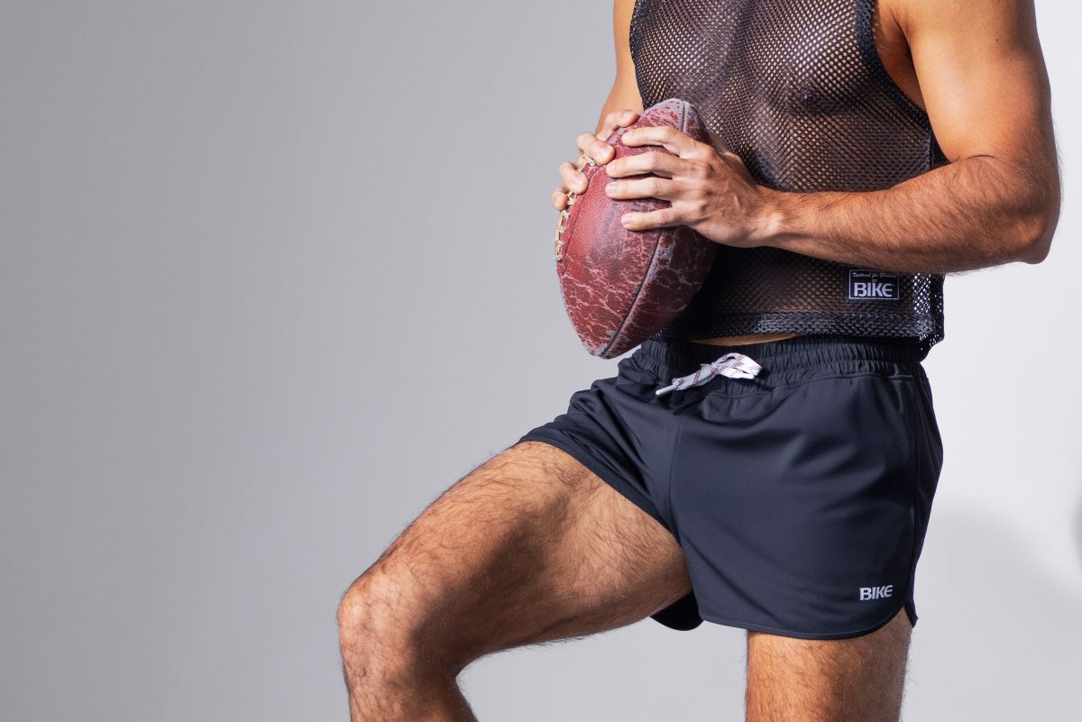 A worn reddish-brown american football with scuff marks shown alongside bike athletic bam200 black track shorts