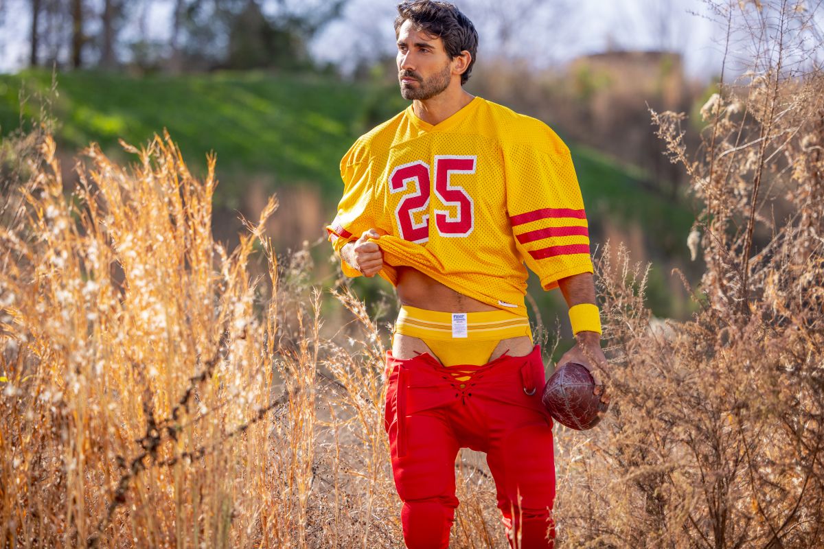 A man wearing a vibrant yellow football jersey with red numerals and stripes paired with red pants showing bike athletic bas306 jockstrap