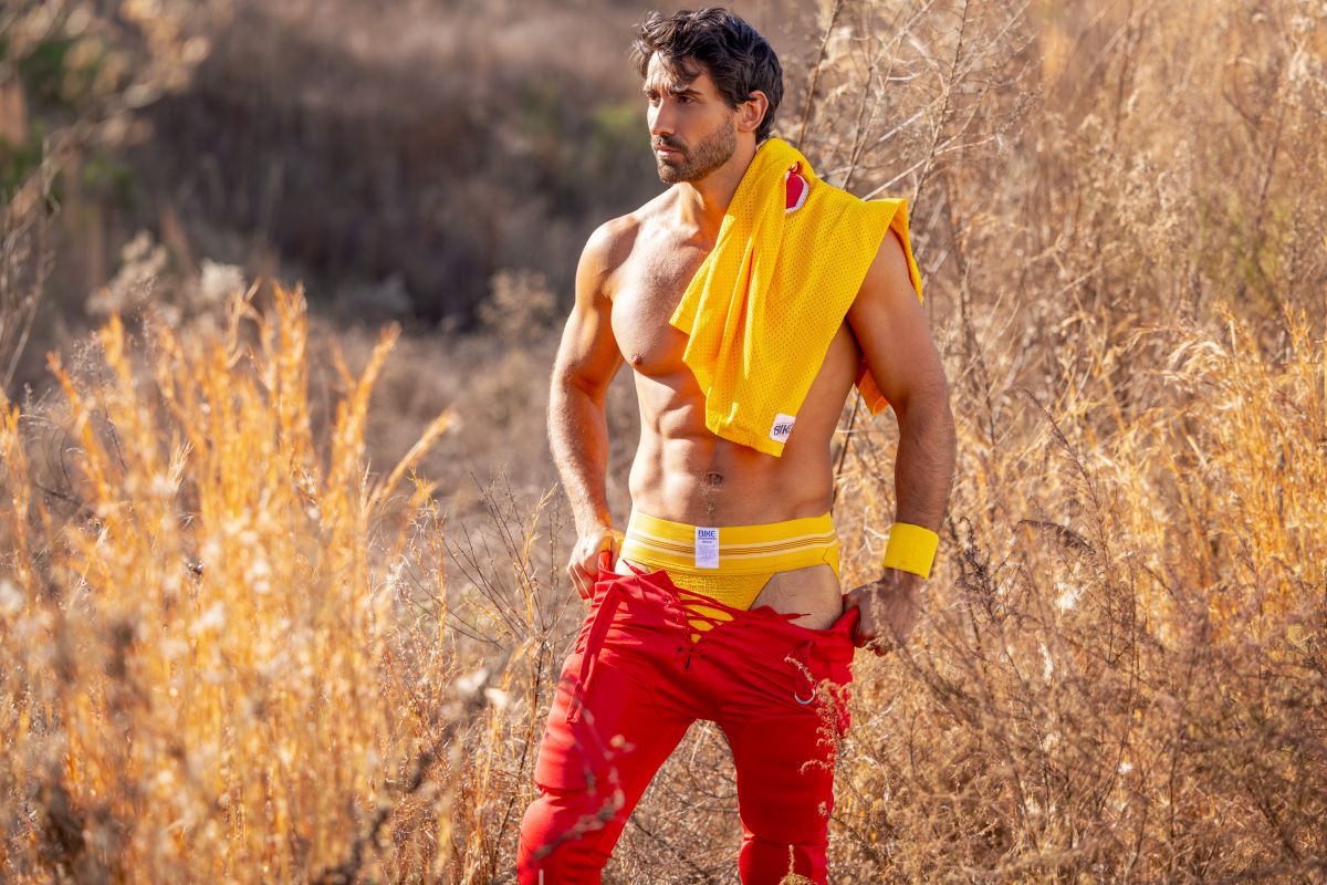A man wearing bright red athletic pants with yellow trim and a yellow bike athletic jockstrap draped over shoulder