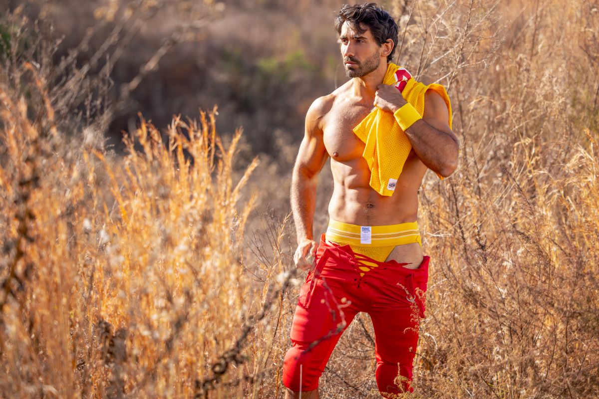 A man wearing a yellow bike athletic jockstrap and bright yellow shirt with red torn shorts showing product fit