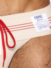 Beige bike brand swim trunks with red drawstring and trim shown with vintage cream bike athletic lace-up jockstrap