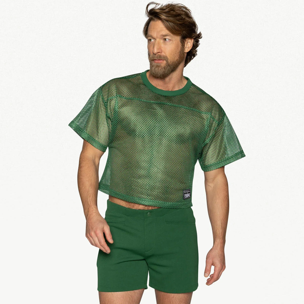 A man wears a green mesh crop-top practice jersey and matching green shorts.