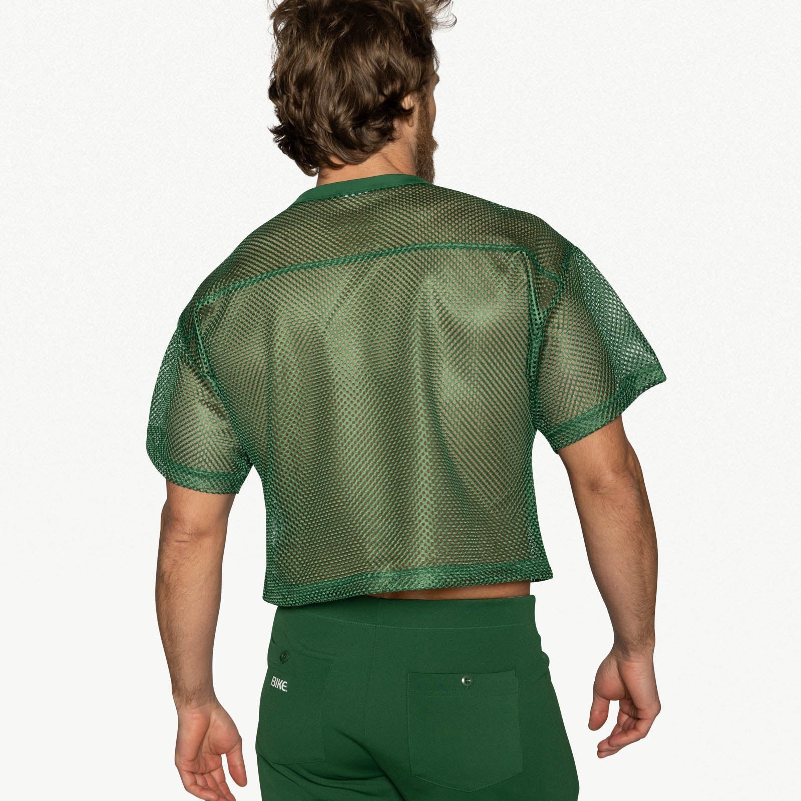 A man from behind wears a green mesh practice jersey and matching green pants.