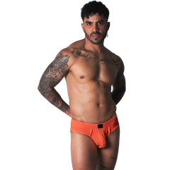 Bright orange athletic mesh jockstrap with a black logo patch on the center waistband, worn by a muscular man.