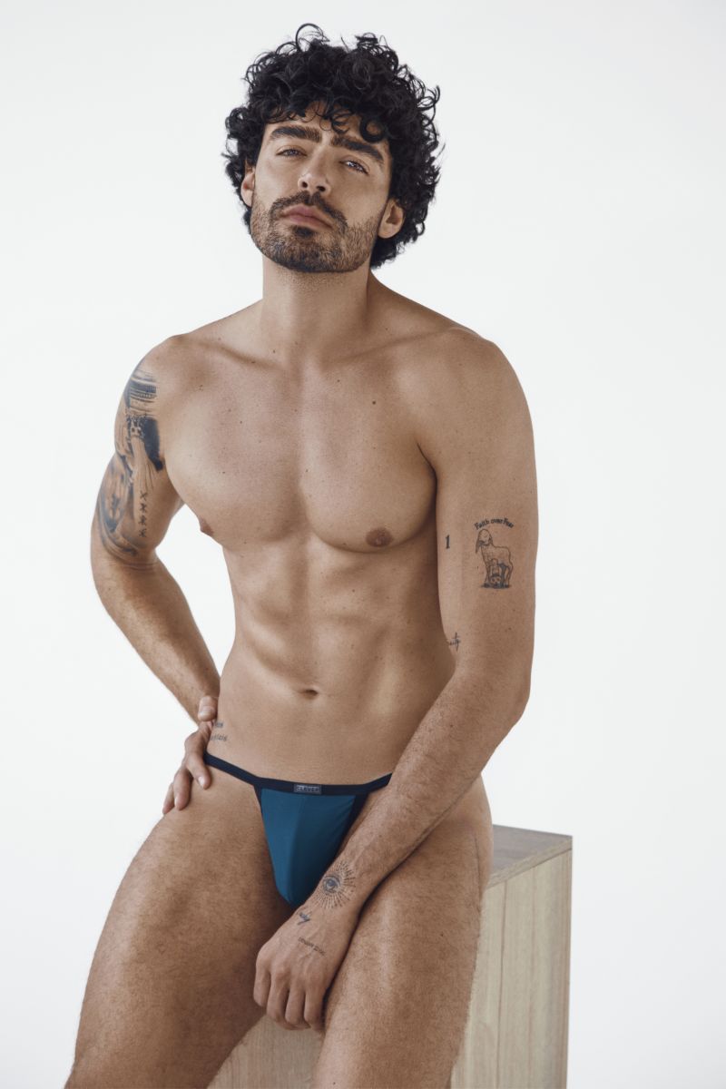 A man wearing Clever Moda petrol blue sleek thongs sitting on a stool.