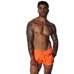 Neon orange mesh athletic shorts with a drawstring waist, modeled by a tattooed man against a black background.
