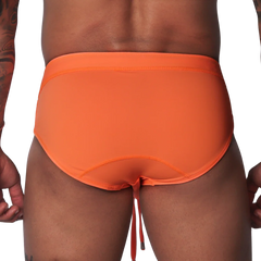 Bright orange swim brief with a wide waistband, contoured back seams, and dangling drawstring against black background.