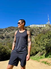 A man wearing the perfect tank black carbon sleeveless tank top and shorts stands on a dirt path near the Hollywood sign