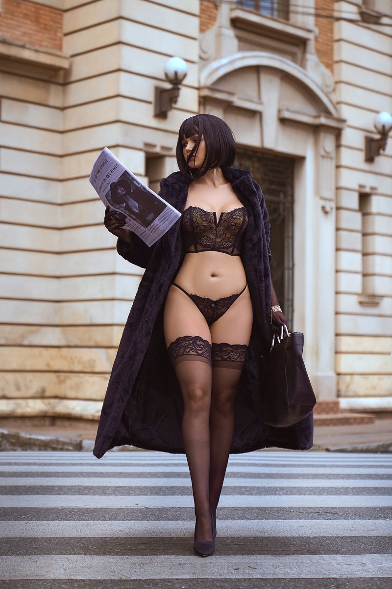 Black lace two-piece lingerie set with strapless bra and matching thong, styled with stockings and coat.