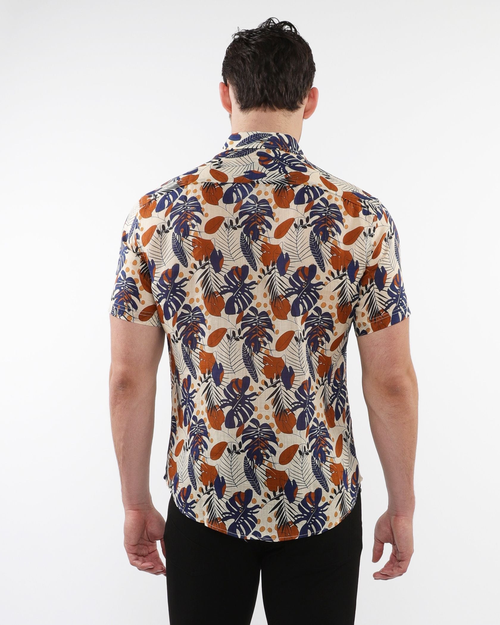 A man wearing a lightweight linen tencel short-sleeved shirt with a navy blue orange and cream tropical pattern on beige