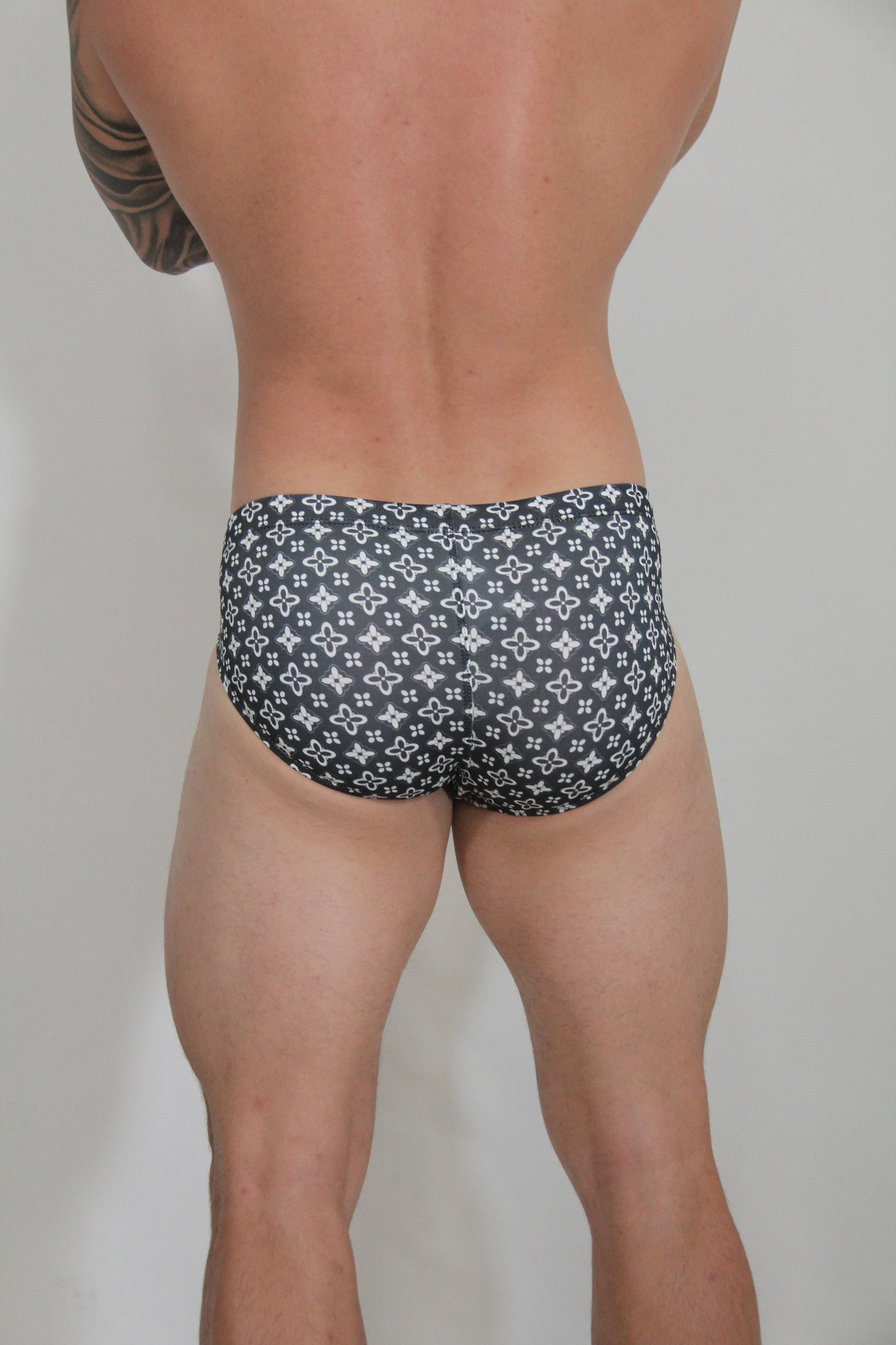 Black swim brief with a repeating white monogram pattern designed for stylish beachwear use