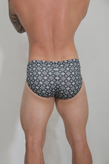 Black swim brief with a repeating white monogram pattern designed for stylish beachwear use