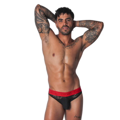 Black lace brief with a red elastic waistband featuring the Gigo logo, worn by a tattooed man.