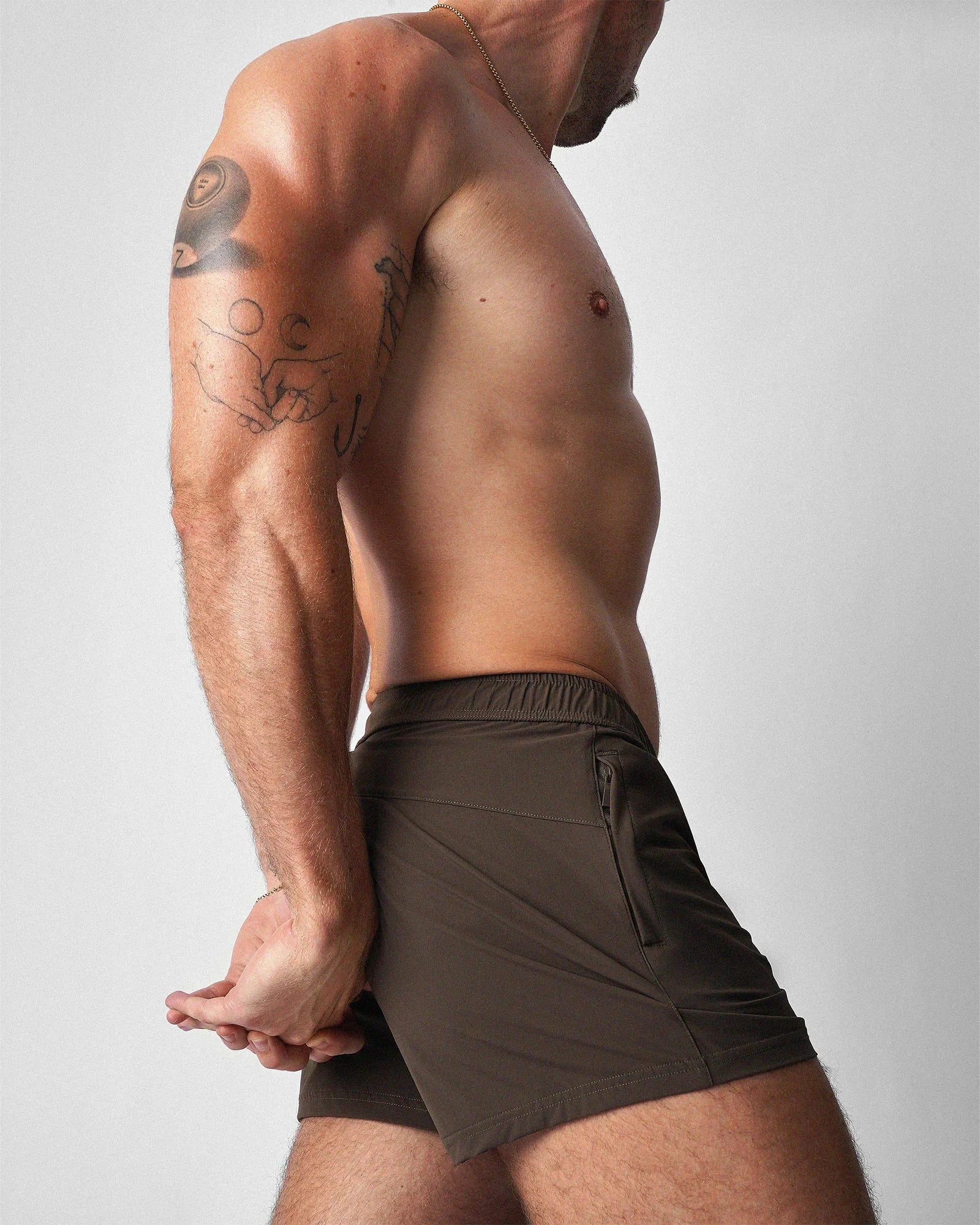 A muscular man stands in profile wearing teamm8 dark olive green gym shorts with a zippered pocket.