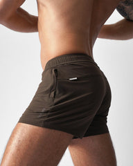 A shirtless man wearing dark brown teamm8 gym shorts, shown from the side against a white background.