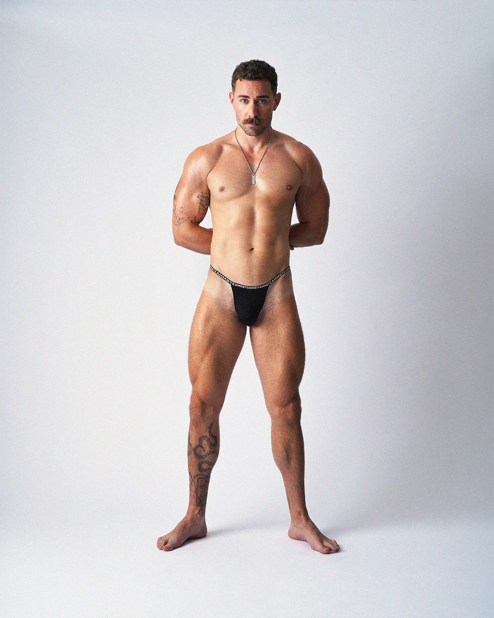 A muscular man wearing black teamm8 Glide Micro Briefs stands facing forward against a plain white background.